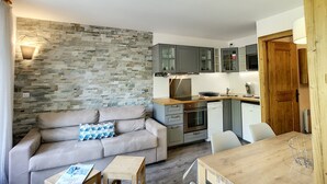 A compact living space with a stone wall, a sofa, a dining table, and a kitchenette.