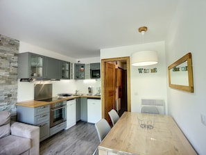 A modern kitchen with grey cabinets, a built-in oven, and a dining area with a wooden table and chairs.