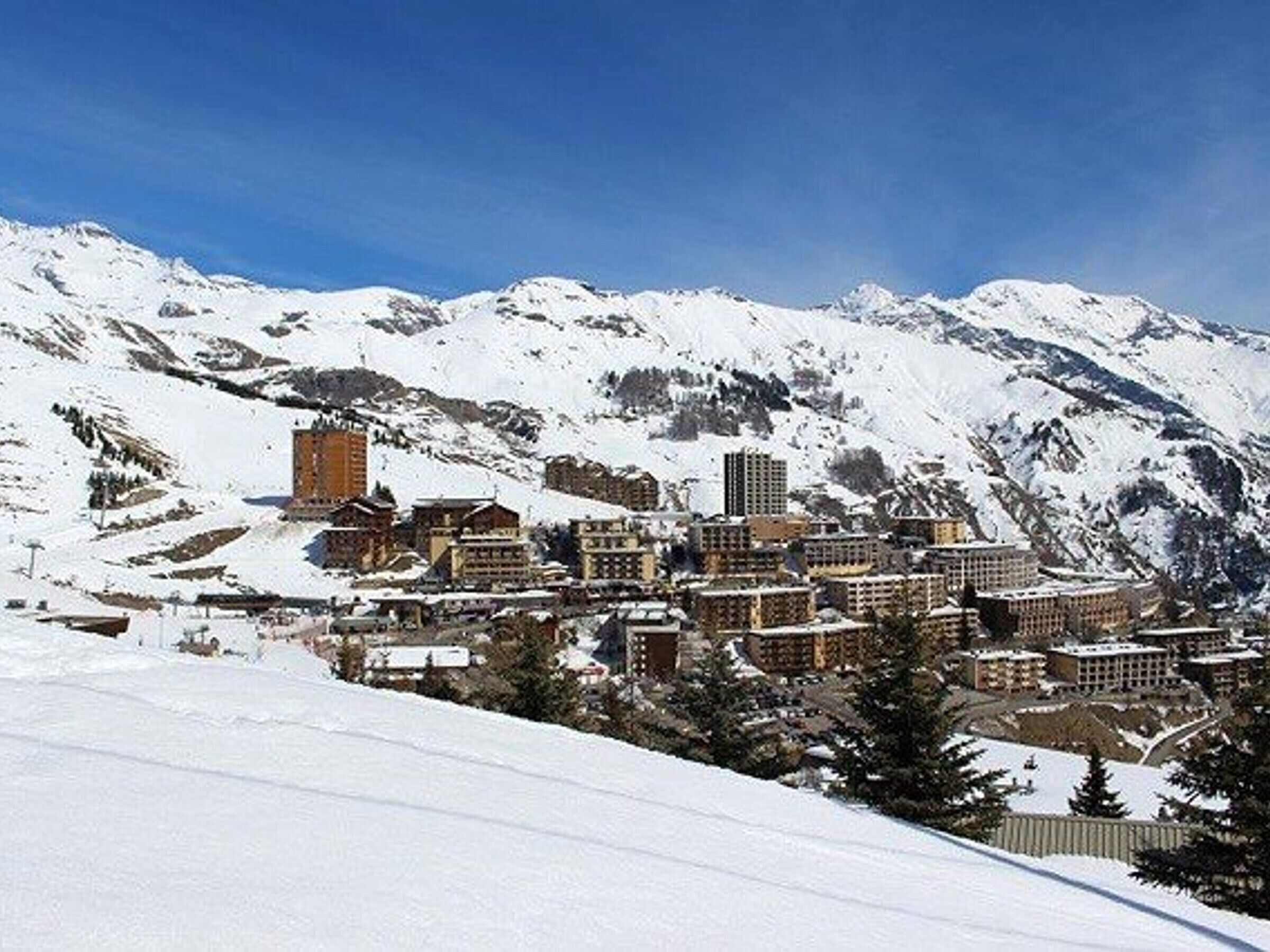 A snow-covered mountain town with buildings clustered together, surrounded by snow-covered mountains.