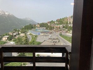 Blick von einem Balkon auf eine gebirgige Landschaft mit Gebäuden, einem Parkplatz und einer Straße.