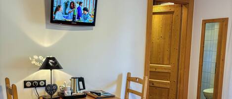 A hotel room with a bed, a desk with a chair, a television, and a wooden door.