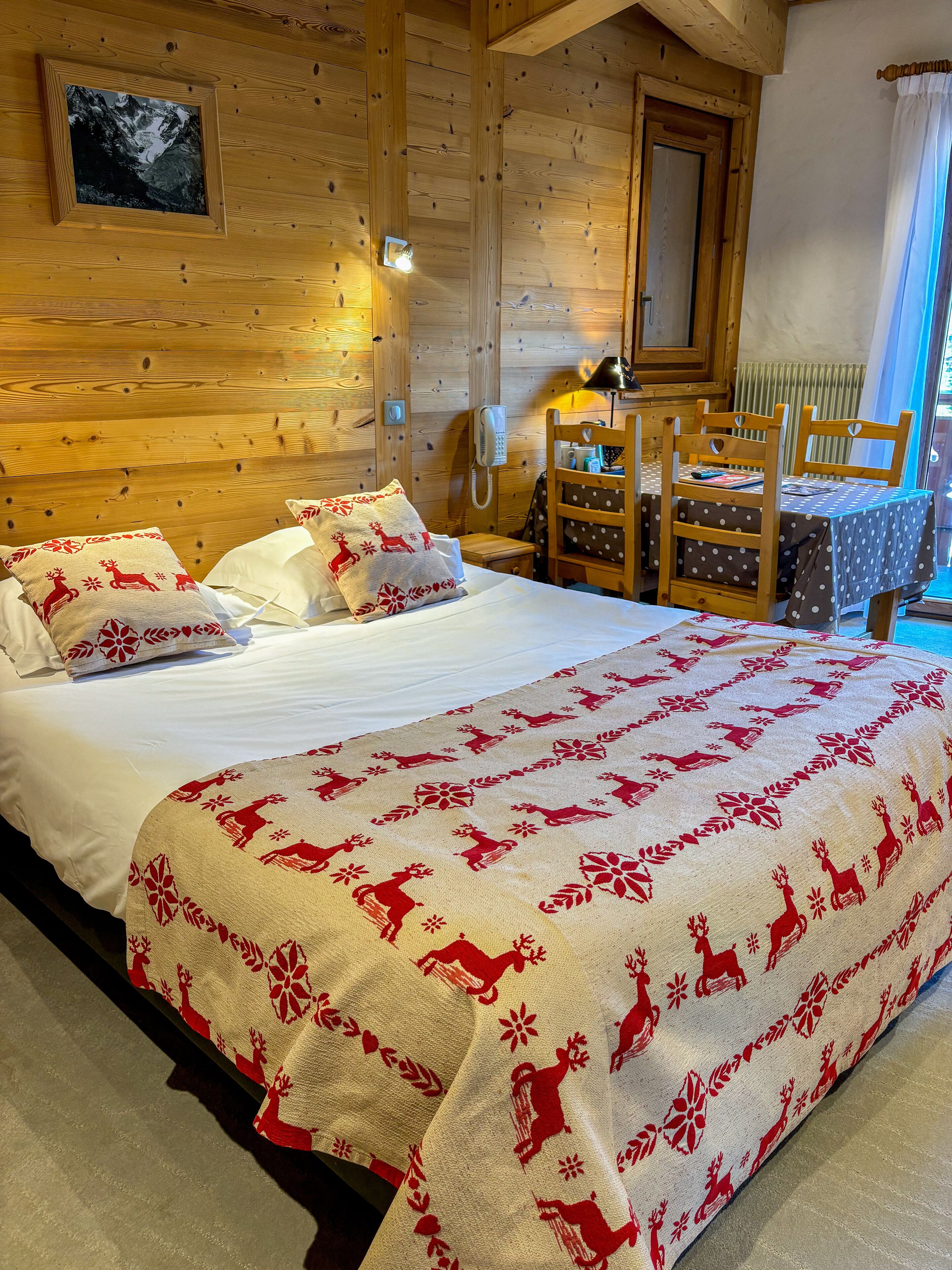 A wooden cabin bedroom with a bed, a small table, and chairs.