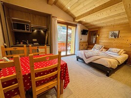 Une pièce confortable comprenant un lit, une table à manger avec des chaises, un coin cuisine et une porte-fenêtre coulissante donnant sur l’extérieur.