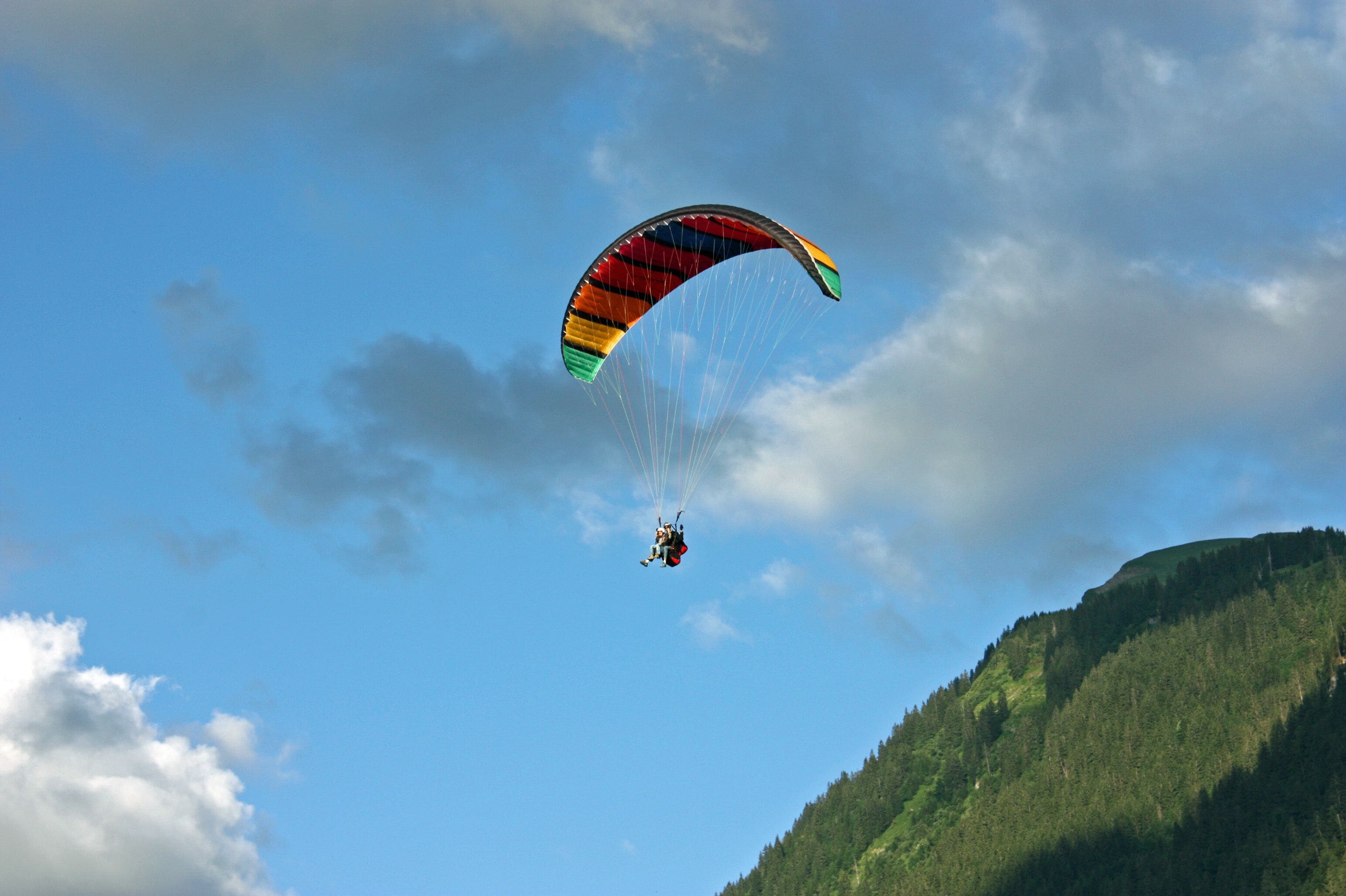 Ein Gleitschirmflieger in der Luft vor blauem Himmel mit einem Berg im Hintergrund.