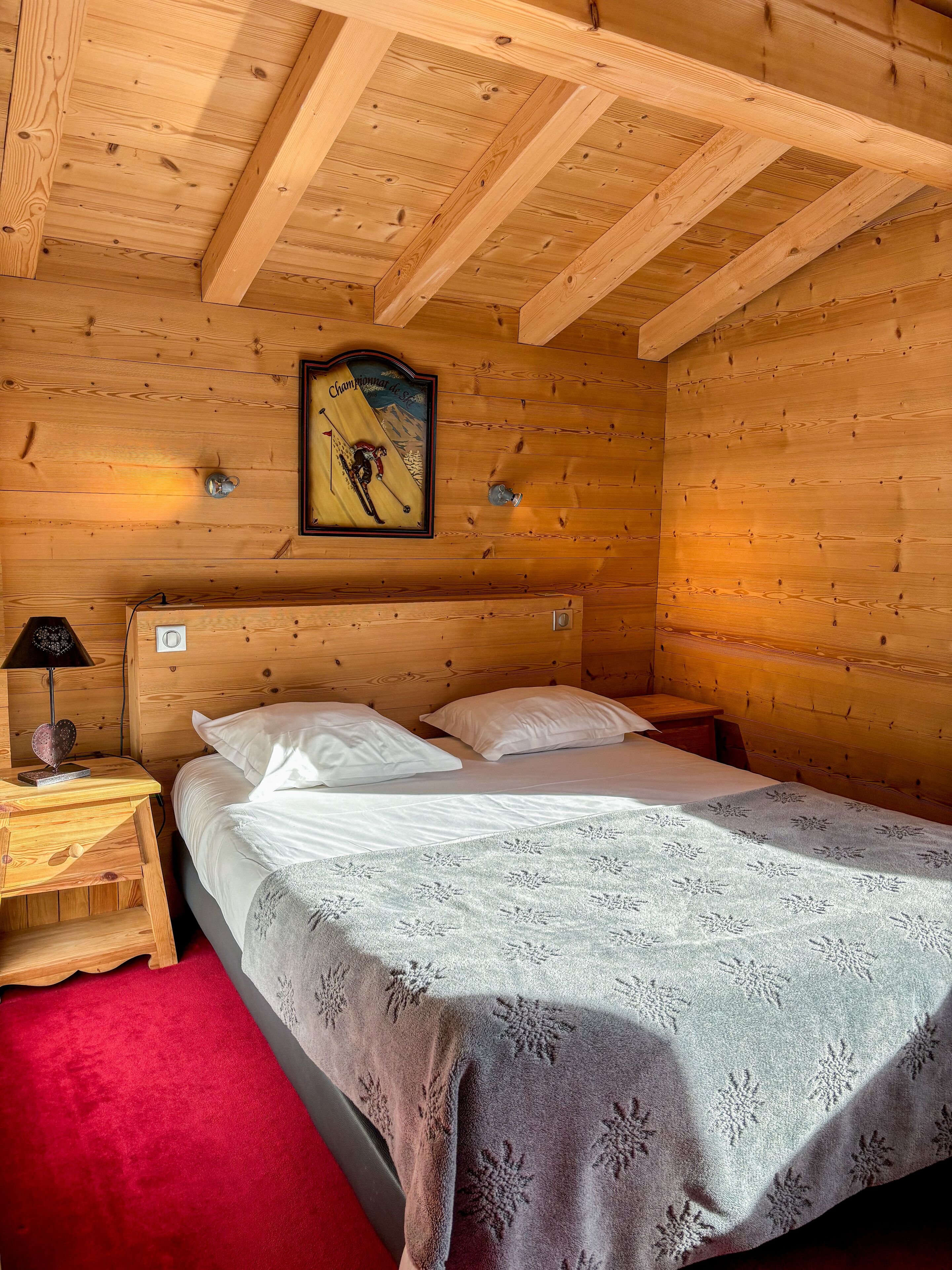 A wooden cabin room with a bed, a nightstand, a lamp, and a framed picture on the wall.