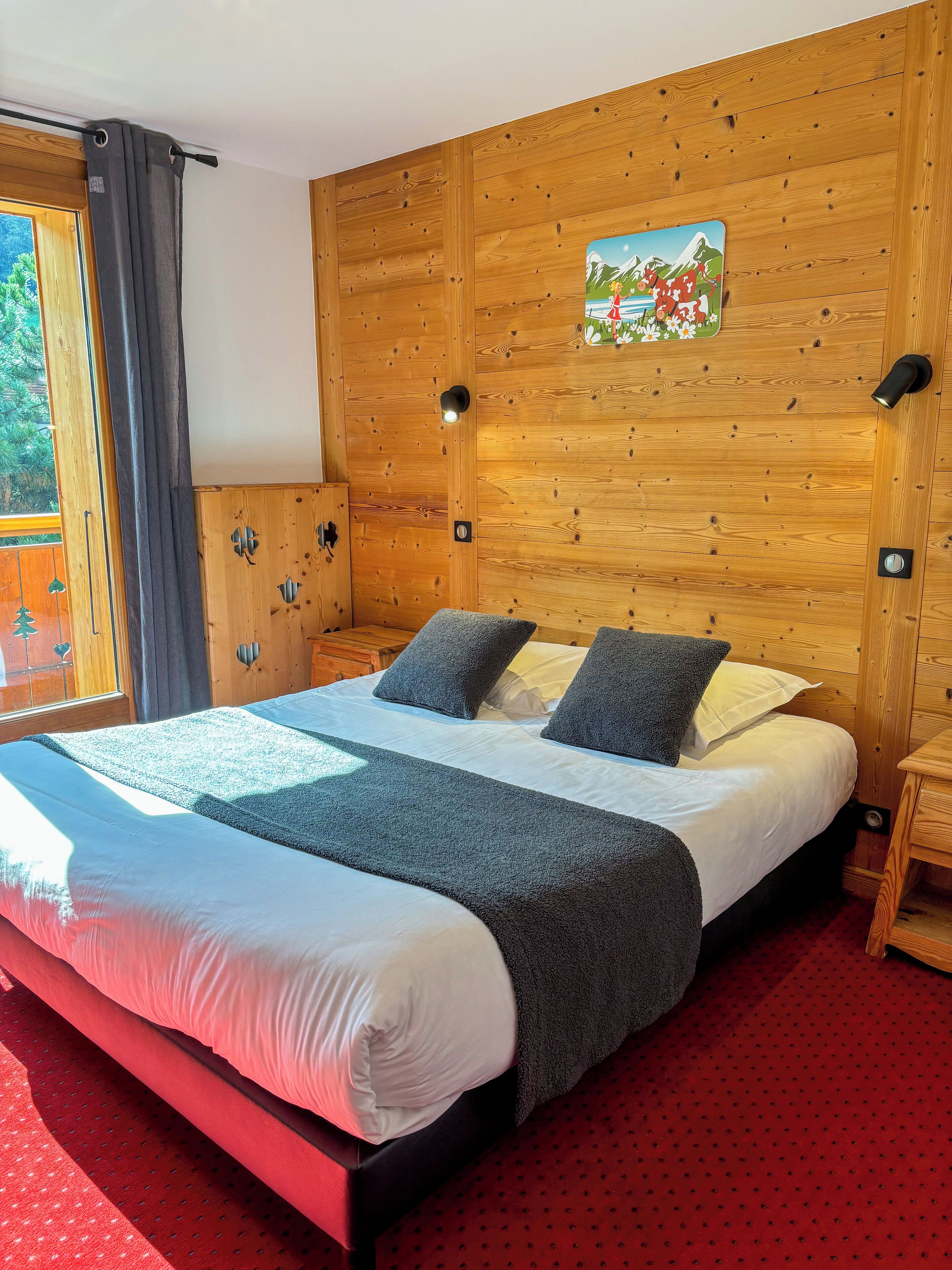 A wooden-paneled room with a large bed, a window with curtains, and a painting on the wall.