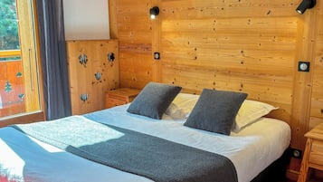 A wooden-paneled room with a large bed, a window with curtains, and a painting on the wall.
