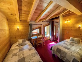 A cozy wooden cabin room with two beds, a desk, and a window.