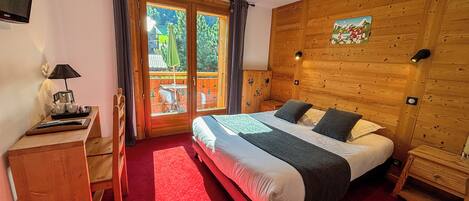 A bedroom with a large bed, a desk with a lamp, a TV, and a sliding glass door leading to an outdoor area.