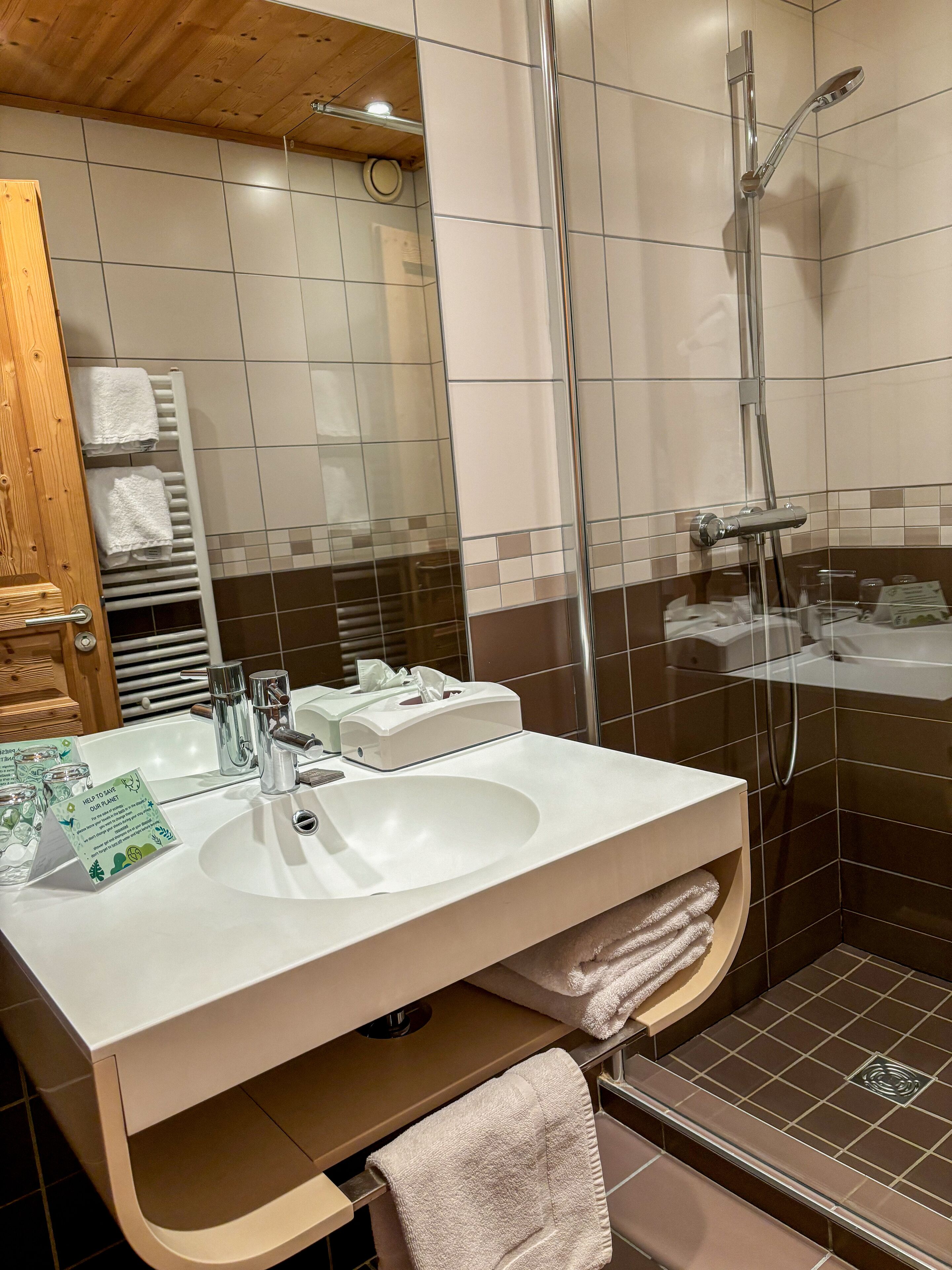 Un baño moderno con un lavabo blanco, cabina de ducha con mampara de vidrio y techo de madera.