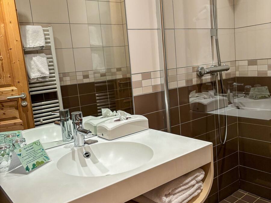 A modern bathroom with a white sink, a glass shower enclosure, and a wooden ceiling.