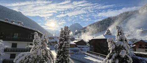 A snowy mountain village with wooden buildings, a clear sky, and a sunlit landscape.