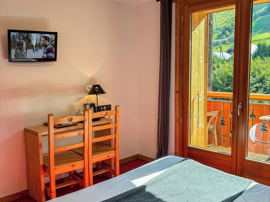 A bedroom with a bed, a wooden desk, a television, and a sliding glass door leading to an outdoor area.