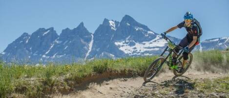 Ciclista de montaña en un sendero de tierra con montañas nevadas al fondo.