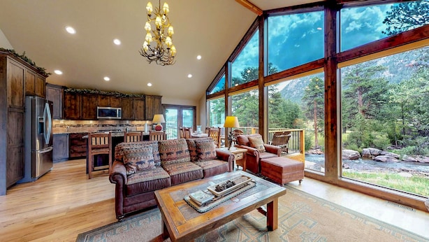 Ein großzügiger Wohnbereich mit einer großen Couch, einem Couchtisch und Blick auf einen Wald durch große Fenster.
