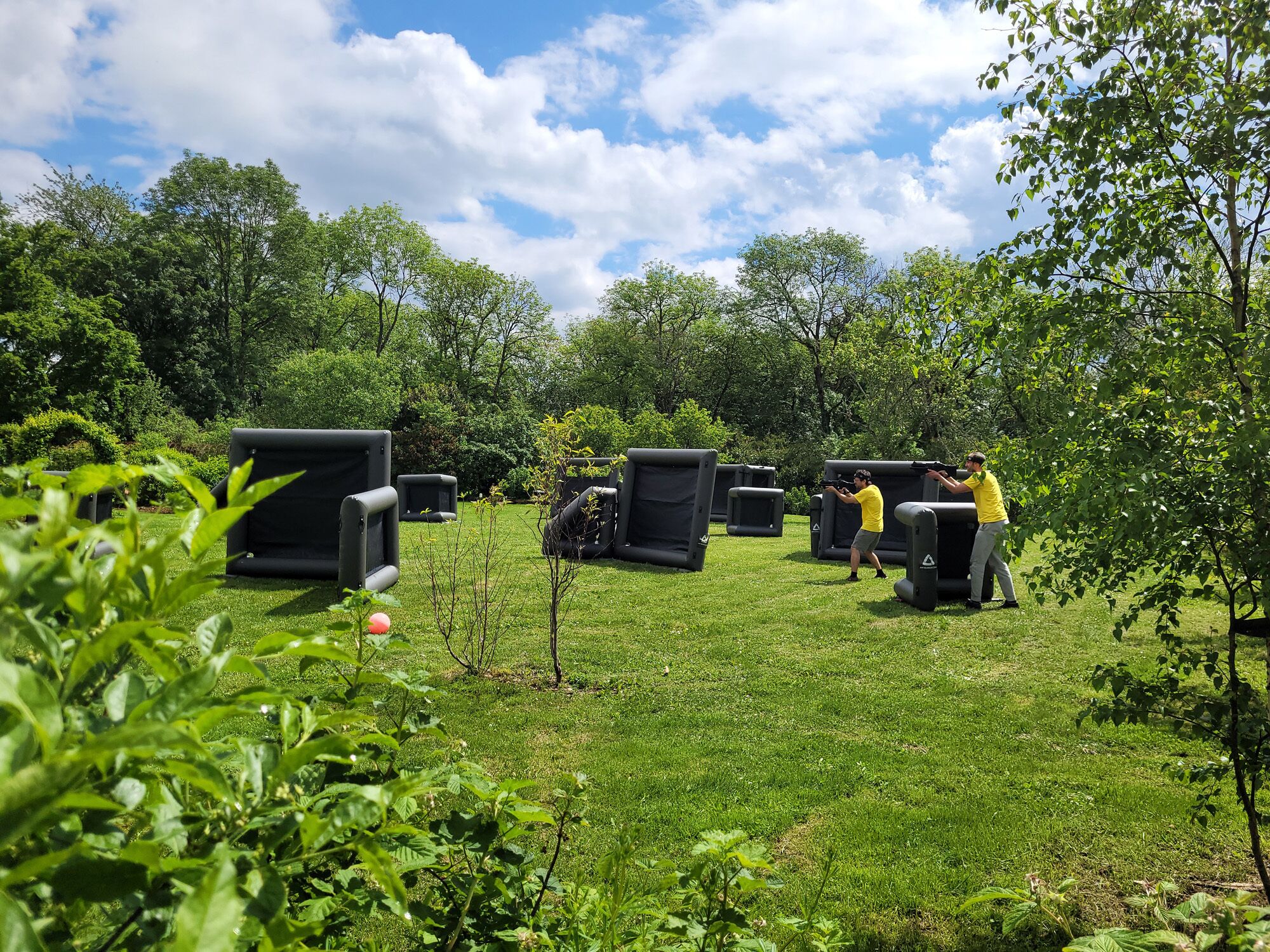 An outdoor shooting range with multiple black inflatable barriers and a person in a yellow shirt aiming a firearm.