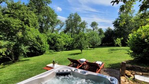 A hot tub in a lush garden with a wooden deck and chairs. - Jardin des Sens (Éguilly)