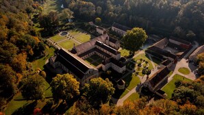 An aerial view of a historic estate with multiple buildings, a central courtyard, and surrounding wooded areas. - Jardin des Sens (Éguilly)