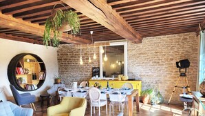 A rustic interior with exposed wooden beams, a stone wall, a round mirror, and a dining area with yellow chairs and a wooden table. - Jardin des Sens (Éguilly)
