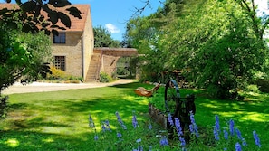 A stone building with a red-tiled roof, a stone staircase, and a garden with blue flowers and a windmill. - Jardin des Sens (Éguilly)