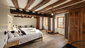 A bedroom with a wooden ceiling, a bed with white bedding, a bedside table, a chair, and a window with curtains. - Jardin des Sens (Éguilly)