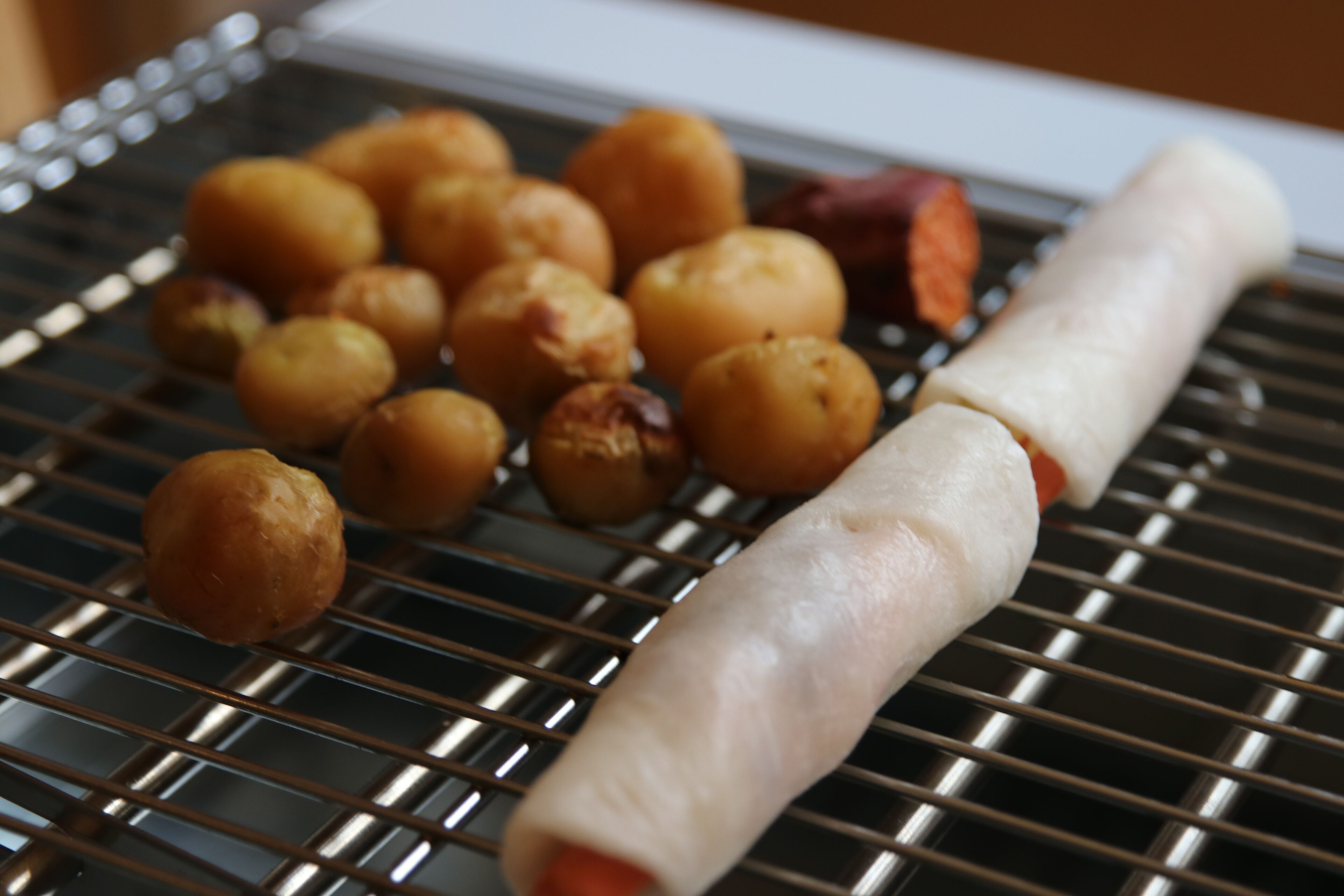 A tray of food items, including sausages and roasted potatoes, on a metal rack.