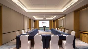 A conference room with a long table, white chairs, and a projector screen displaying the Hilton Garden Inn logo.