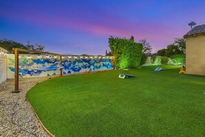 A well-maintained backyard with artificial grass, a hammock, and a wall with a mural. - Azul: Pool, Spa, Fire Pit and Pickle Ball Court! (Indio)