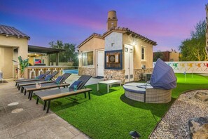 A poolside area with lounge chairs, a barbecue grill, and a stone wall with a dartboard. - Azul: Pool, Spa, Fire Pit and Pickle Ball Court! (Indio)
