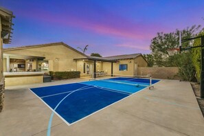 A tennis court with a net, adjacent to a building with a bar area. - Azul: Pool, Spa, Fire Pit and Pickle Ball Court! (Indio)