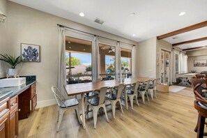A spacious kitchen with a large dining table, wooden cabinets, and a view of the outdoors. - Azul: Pool, Spa, Fire Pit and Pickle Ball Court! (Indio)