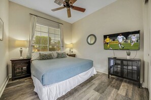 A bedroom with a bed, a ceiling fan, a television, and a nightstand with a lamp. - Azul: Pool, Spa, Fire Pit and Pickle Ball Court! (Indio)