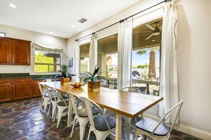 A spacious kitchen with a large dining table, white chairs, and wooden cabinets. - Azul: Pool, Spa, Fire Pit and Pickle Ball Court! (Indio)