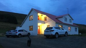 A two-story house with a red roof, two parked cars, and a dog walking on the driveway. - Öndólfsstaðir Farm B&B (Laugar)