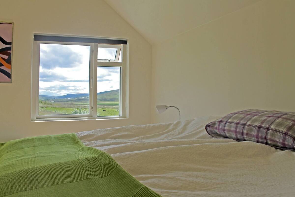 Un dormitorio con cama, ventana y vista al paisaje, además de una lámpara.