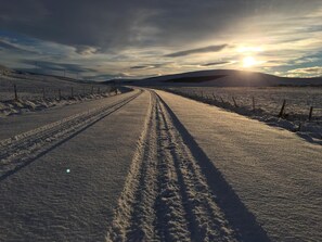 Una strada innevata con tracce di pneumatici che conducono verso il sole.