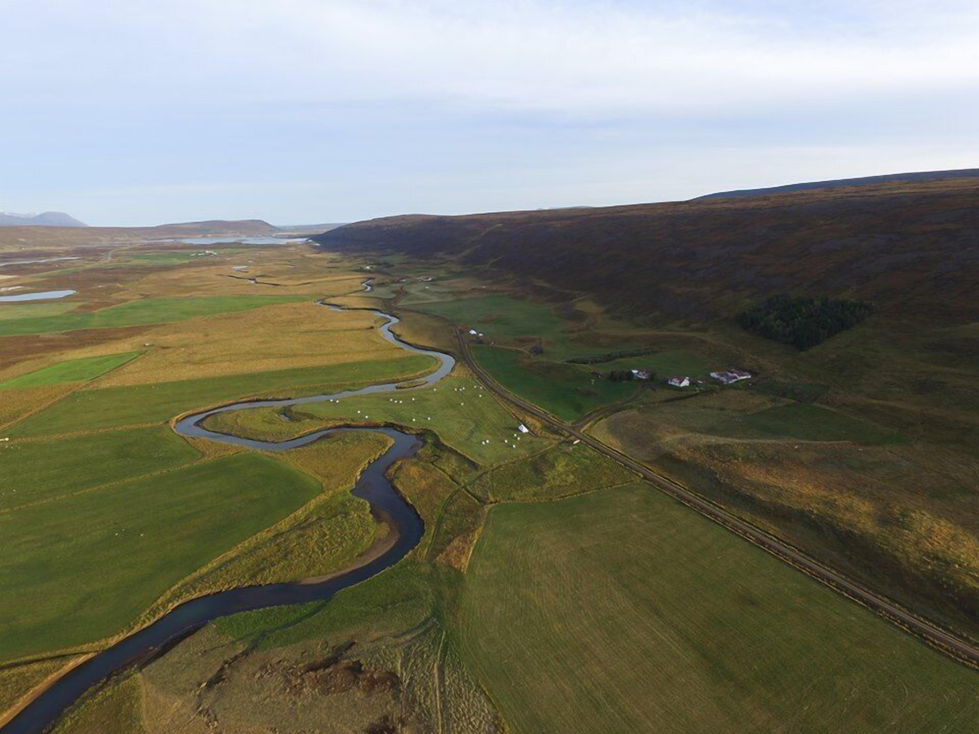 Vista aérea de un paisaje rural con un río sinuoso, campos verdes y edificios dispersos.