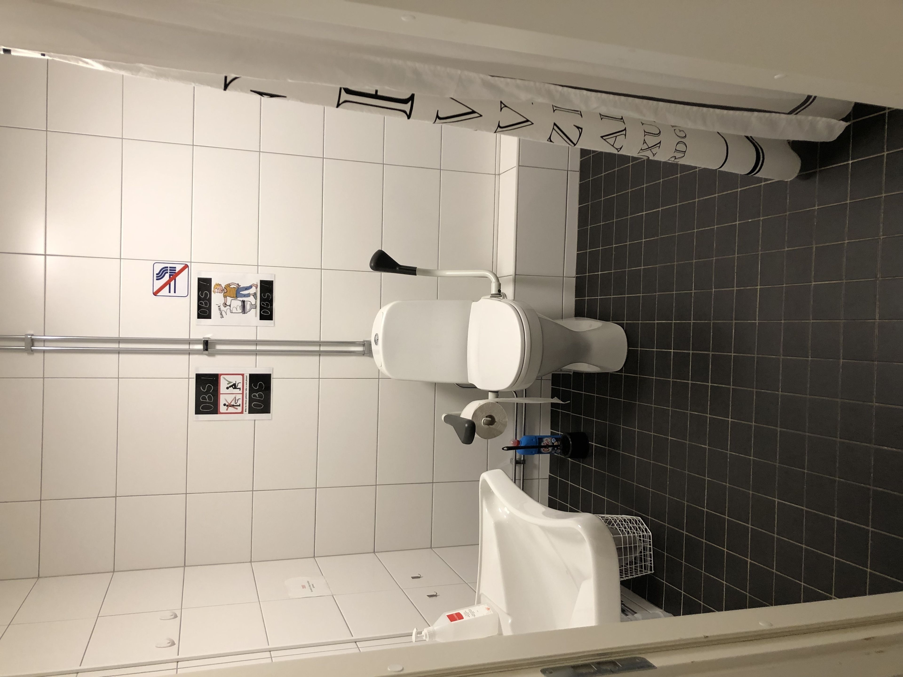 A bathroom with white tiles, a toilet, a hand dryer, and a towel rack.