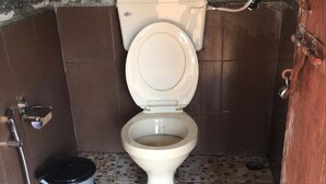 Un baño pequeño con azulejos, un inodoro, un balde y una ducha.