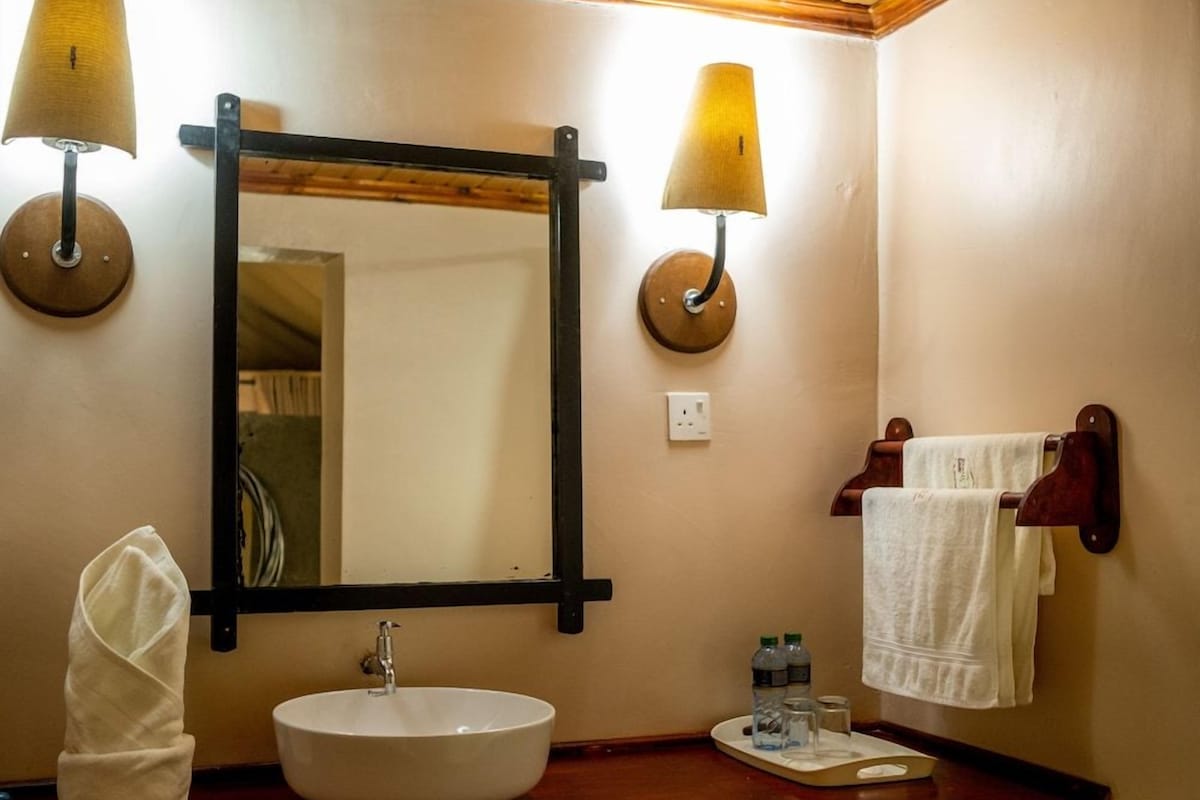A bathroom with a round sink, two wall-mounted lamps, a mirror, and a towel rack.