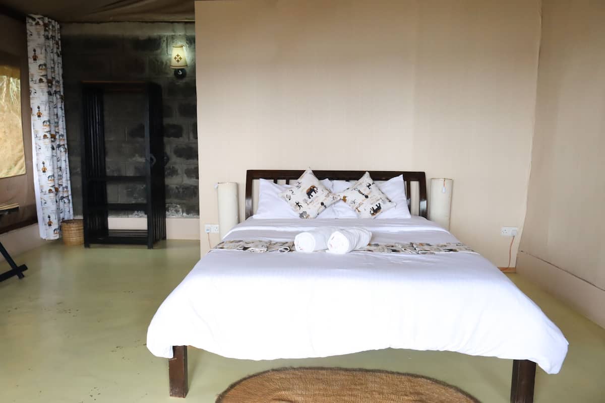 A neatly made bed with white linens and decorative pillows, a wooden headboard, a wall-mounted light fixture, and a door leading to another room.