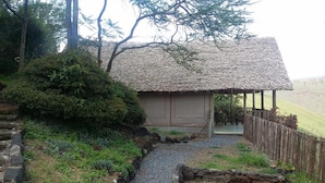 A rustic thatched-roof structure with a stone pathway leading to a wooden fence. - Maili Saba Camp (Nakuru)