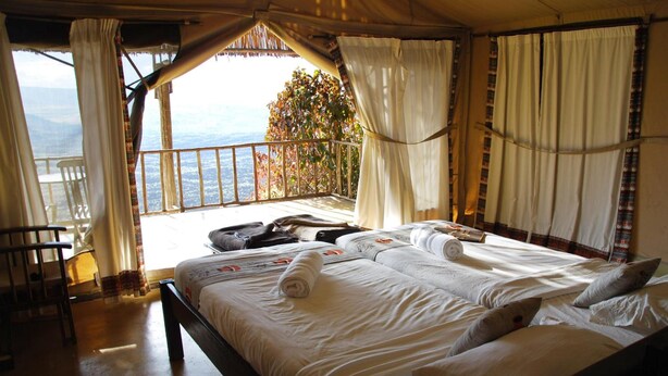 A bedroom with a large bed, a chair, and a balcony with a view. - Maili Saba Camp (Nakuru)