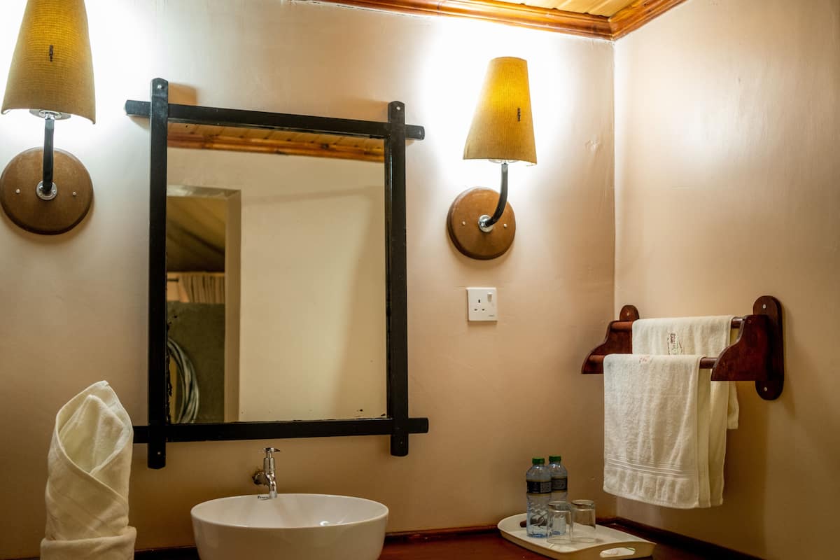 A bathroom with a round sink, two wall-mounted lamps, a mirror, and a towel rack with towels.