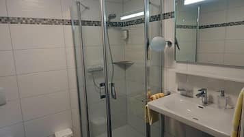 A modern bathroom with a glass-enclosed shower, a white sink with a mirror above it, and a tiled floor.