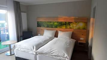 A hotel room with a double bed, a small round table, a view of the outdoors, and a painting on the wall.