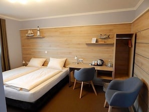 A hotel room with a bed, a desk, two chairs, a wardrobe, and a shelf with decorative items. - Hotel Garni Haaster Krug Otte (Grossenkneten)
