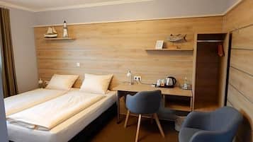 A hotel room with a bed, a desk, two chairs, a wardrobe, and a shelf with decorative items.