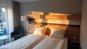 A hotel room with two beds, a desk, a chair, and a view of the outdoors.