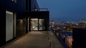 Ein modernes Gebäude mit einem Balkon, der auf eine Stadtlandschaft zum Abend hin blickt.